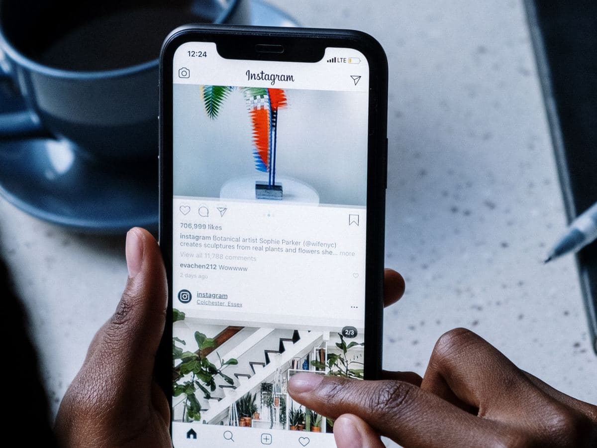 Person scrolling an Instagram feed on a phone at a café table